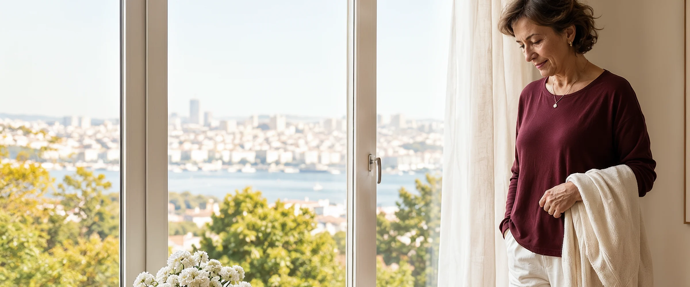 Aydınlık bir evde pencere yanında oturan 50+ kadın; kemik gücü, kırık riski ve koruyucu ortopedik takip yazısı için sakin editoryal kart görseli